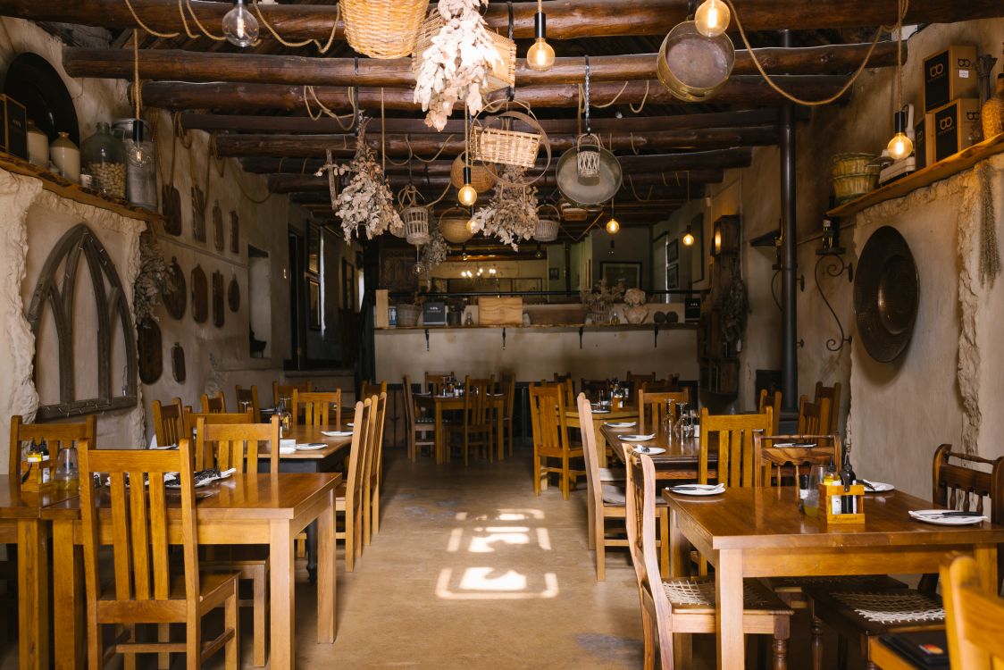 Rustikal eingerichtete kleine Pizzeria auf dem Weingut Under Oaks in Südafrika mit Holztischen, warmem Licht und gemütlicher Atmosphäre.