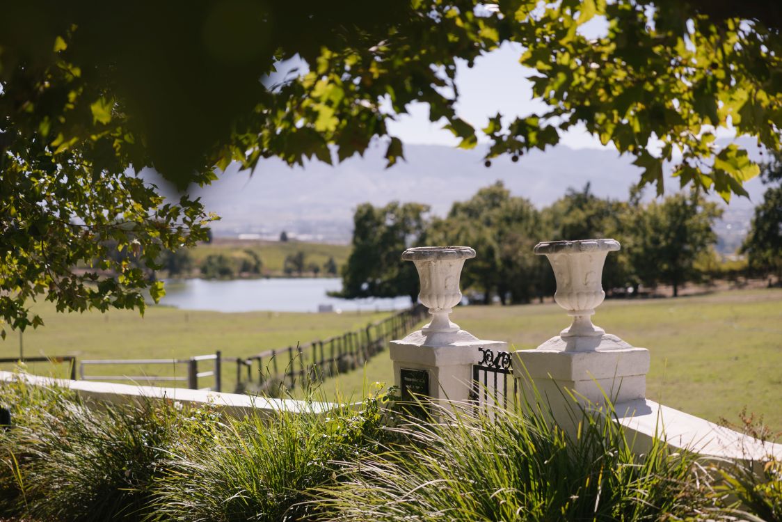 Landschaftsaufnahme des Weinguts Under Oaks in Südafrika mit Blick über Wiesen, Bäume, Wasser und das Gelände des Weinguts.